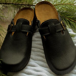 May include: A pair of black leather slip-on clogs with a buckle strap and a brown insole.