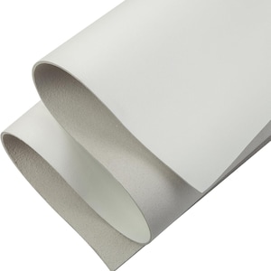 May include: Close-up of two sheets of white leather, one partially folded over the other. The top sheet is smooth and bright white, while the underside of the folded sheet is a light gray. The edges of the leather are visible.