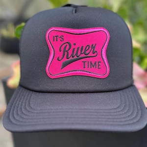 Puede incluir: Gorra de camionero negra con un parche rosa que dice "It's River Time". La gorra tiene una parte delantera estructurada y una parte trasera de malla, ideal para actividades al aire libre.