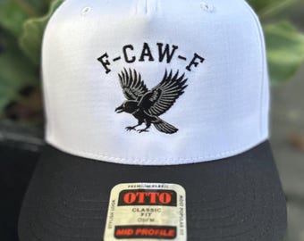 May include: A white and black baseball cap with the text "F-CAW-F" and a black raven graphic. The cap has a black brim and a "OTTO" label. The cap is a mid-profile, classic fit.
