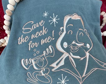 Może przedstawiać: Turkusowa bluza z białym haftem. Haft przedstawia kreskówkowego mężczyznę z wąsem i renifera. Tekst "Save the neck for me!" jest wyszyty na biało.