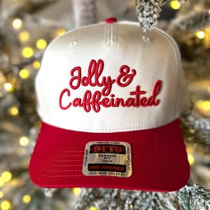 May include: A white and red baseball cap with the embroidered text "Jolly & Caffeinated" in red script. The cap has a red brim and a tag that reads "OTTO CLASSIC FIT OSFM MID PROFILE".