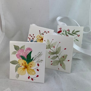 May include: Four watercolor cards with floral designs. The cards are white with a variety of flowers and leaves painted in shades of pink, yellow, green, and red.