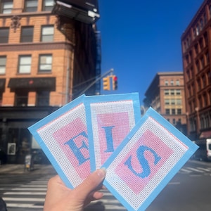 Könnte beinhalten: Drei blaue und rosa Filzquadrate mit den Buchstaben "F.I.S." in Weiß auf jedem Quadrat gestickt.