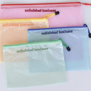 Può includere: Quattro buste con cerniera a rete rosa, gialle, blu e verdi. Ogni busta ha una cerniera colorata e il testo "unfinished business" stampato sopra. Le buste sono disposte a strati.