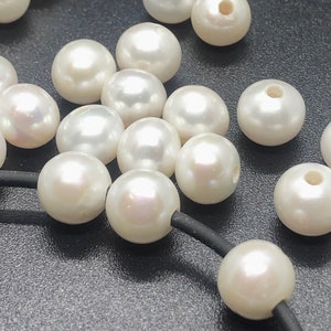 May include: A collection of white pearl beads with a hole in the center. The beads are arranged on a black surface.