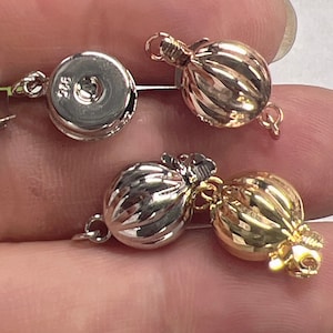 Może przedstawiać: Trzy zapięcia do pereł w kolorze srebrnym, złotym i różowym złocie. Każde zapięcie ma okrągły, fakturowany wzór i zapięcie na haczyk.