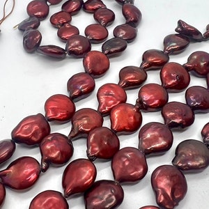 Puede incluir: Una hebra de perlas de agua dulce de color rojo oscuro con una forma ligeramente irregular. Las perlas están enhebradas en un cordón fino y están listas para ser utilizadas en la elaboración de joyas.