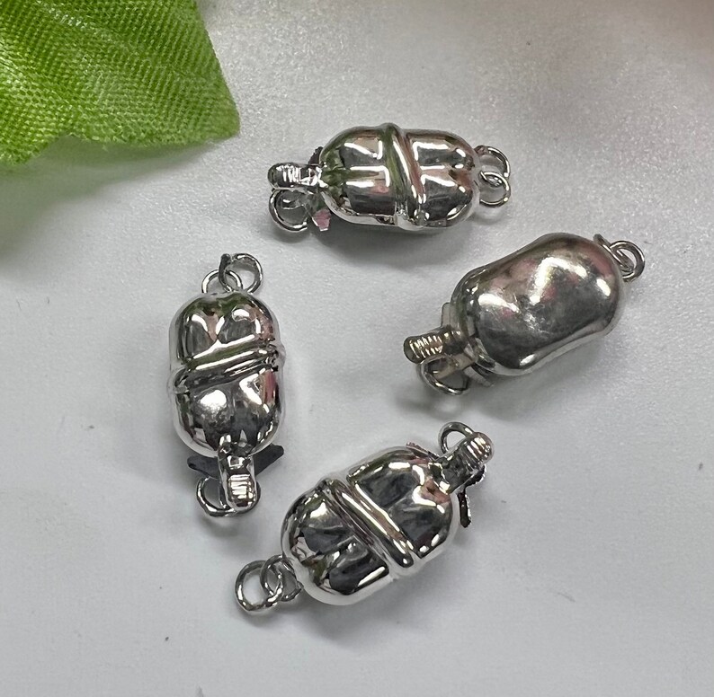 May include: Four silver-toned metal clasps for necklaces or bracelets. Each clasp has a rounded, barrel-shaped design with a decorative groove.
