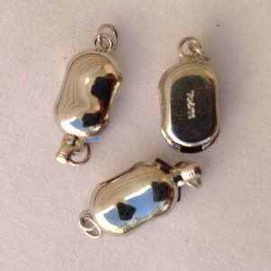 May include: Three silver-toned metal bottle stoppers. The stoppers are shaped like small, elongated bottles with a loop at the top for hanging. One stopper has the word "Barrel" engraved on the bottom.