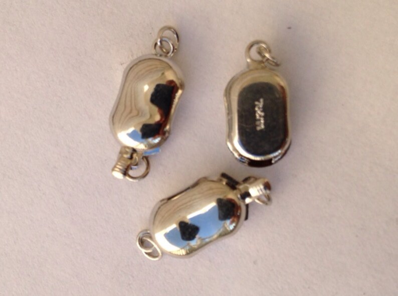 May include: Three silver-toned metal bottle stoppers. The stoppers are shaped like small, elongated bottles with a loop at the top for hanging. One stopper has the word "Barrel" engraved on the bottom.