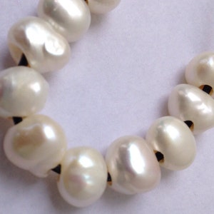 May include: A strand of white pearl beads on a black cord. The pearls are round and have a smooth, glossy finish.