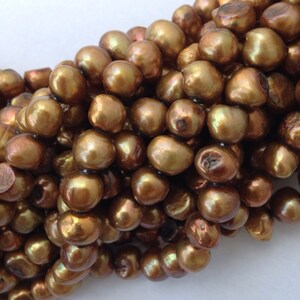 May include: A strand of golden brown pearls, each pearl is round and smooth with a slight iridescent sheen.