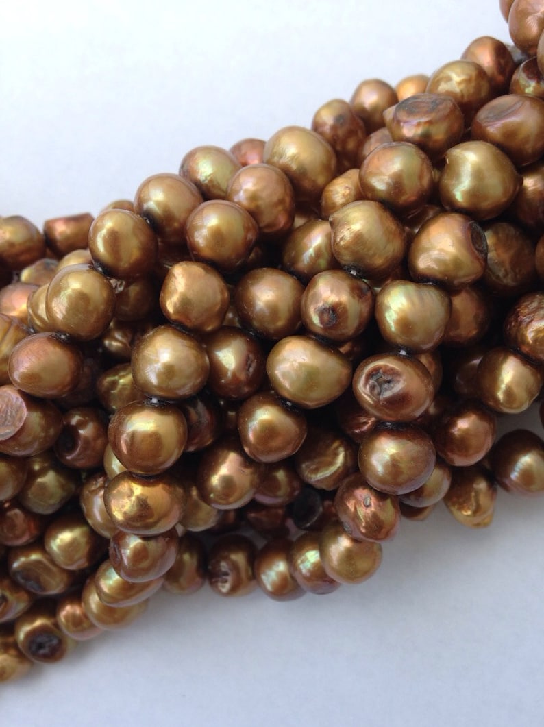May include: A strand of golden brown pearls, each pearl is round and smooth with a slight iridescent sheen.
