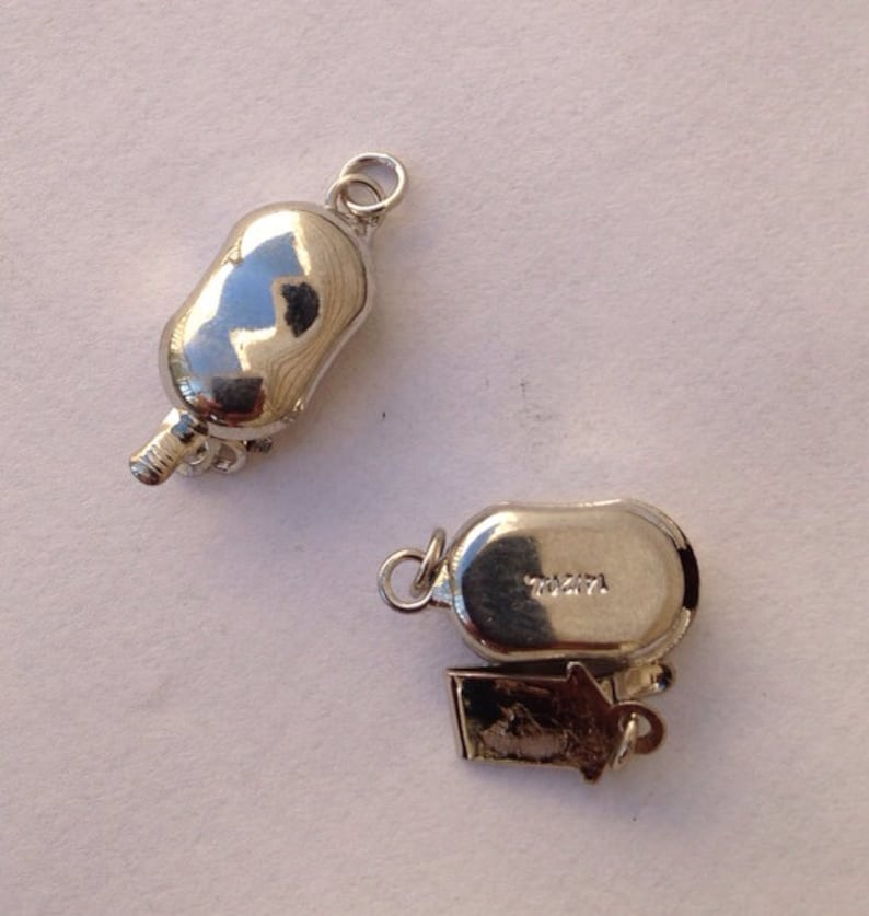 May include: Two silver-toned metal clasps for a necklace or bracelet. One clasp has a small, decorative charm attached. The clasp on the right has the number "70271" engraved on it.