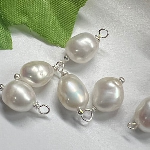 May include: Six white freshwater pearls with silver jump rings. The pearls are oval shaped and have a smooth, glossy finish.