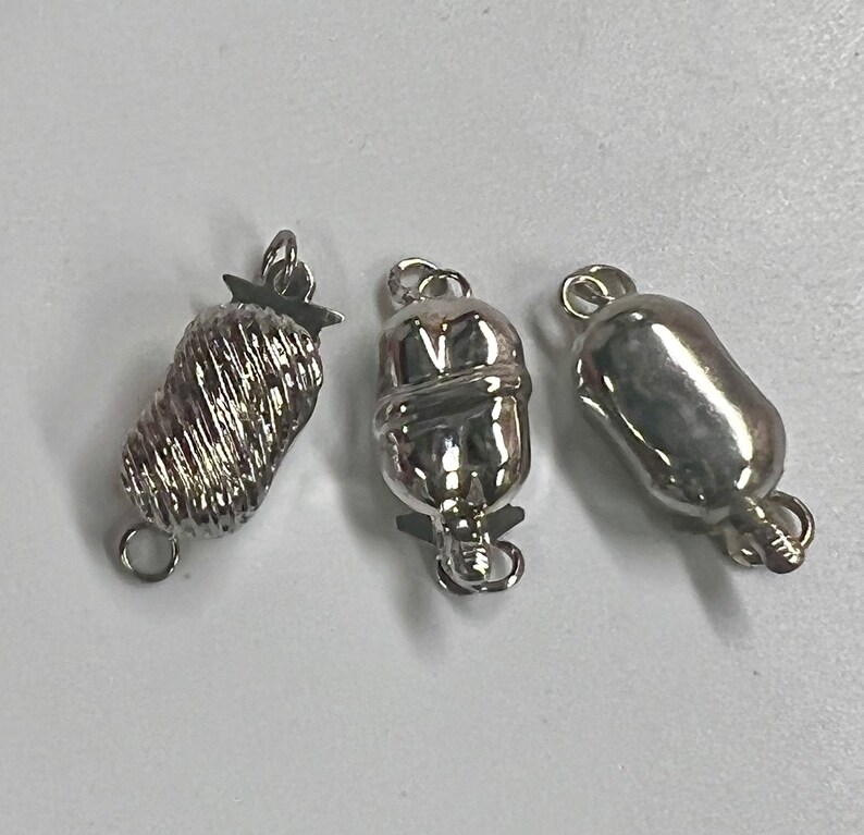 May include: Three silver-toned clasps for necklaces or bracelets. The clasps are different styles, one is a twisted design, one is a smooth oval, and one is a textured oval.