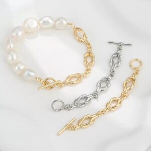 K&ouml;nnte beinhalten: Zwei Armb&auml;nder mit Knotendesign. Ein Armband ist golden und hat eine Reihe wei&szlig;er Perlen. Das andere Armband ist silber.