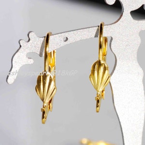 May include: A pair of gold-tone earring hooks with a shell-shaped design. The hooks are made of metal and have a shiny finish.