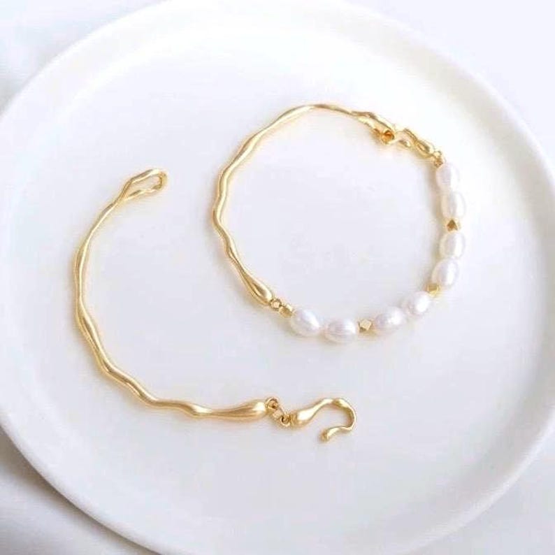 May include: Two gold bracelets, one with a simple wavy design and the other with a row of white pearls.
