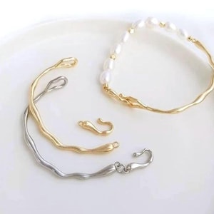 May include: Two gold and silver bracelets with a wavy design. The gold bracelet has a pearl and gold chain attached to it. There are two gold clasps.