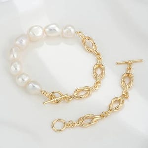 K&ouml;nnte beinhalten: Ein goldenes Kettenarmband mit Knotendesign und einer Reihe wei&szlig;er Perlen. Das Armband hat einen Schiebeverschluss.