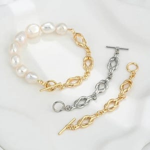 K&ouml;nnte beinhalten: Zwei Armb&auml;nder, eines mit einer goldenen Kette und einer Reihe wei&szlig;er Perlen, das andere mit einer silbernen Kette. Beide Armb&auml;nder haben einen Schiebeverschluss.