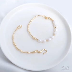 May include: Two gold bracelets, one with a simple curved design and the other with a row of white pearls.