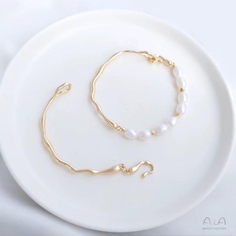 May include: Two gold bracelets, one with a simple curved design and the other with a row of white pearls.