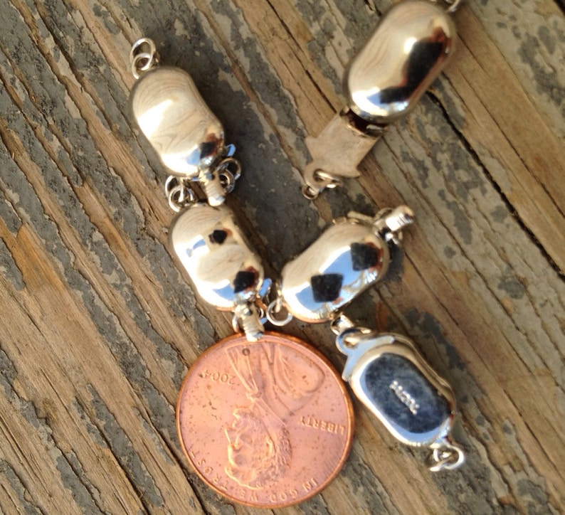May include: A silver charm bracelet with a variety of silver charms, including a round charm with the inscription "925". The bracelet is lying on a wooden surface next to a US penny.