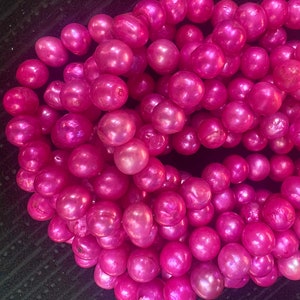 Op de afbeelding: Een streng roze, iriserende parels. De parels zijn rond en glad en hebben een subtiele glans.