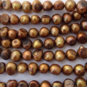 May include: A strand of brown freshwater pearls. The pearls are round and have a slight iridescent sheen.