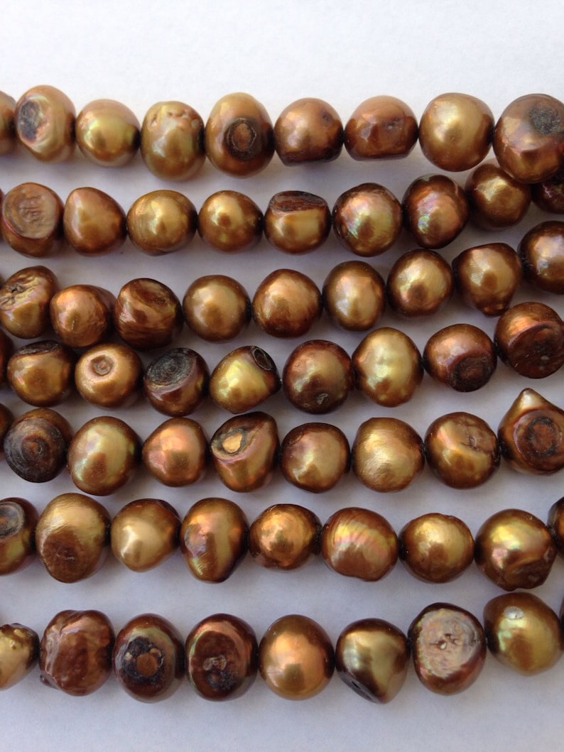 May include: A strand of brown freshwater pearls. The pearls are round and have a slight iridescent sheen.
