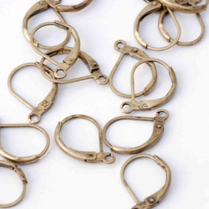 May include: A group of gold-toned earring hooks, also known as ear wires, are scattered on a white surface. The hooks are made of metal and have a teardrop shape.