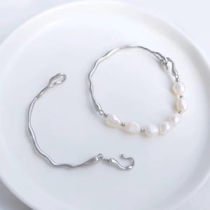 May include: Two silver bracelets with a delicate, irregular design. One bracelet features a row of white pearls.