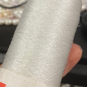 May include: A spool of white iridescent thread.