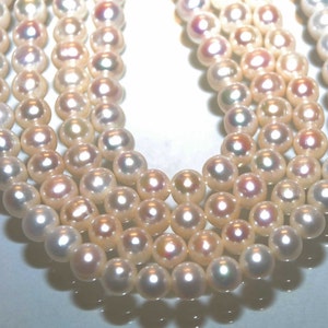 May include: A strand of white pearls with a slight iridescent sheen. The pearls are round and smooth, and they are strung on a white thread.
