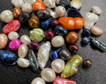 May include: A collection of various colored pearls, including white, pink, orange, green, blue, and black. The pearls are of different shapes and sizes, and some have a pearlescent sheen.