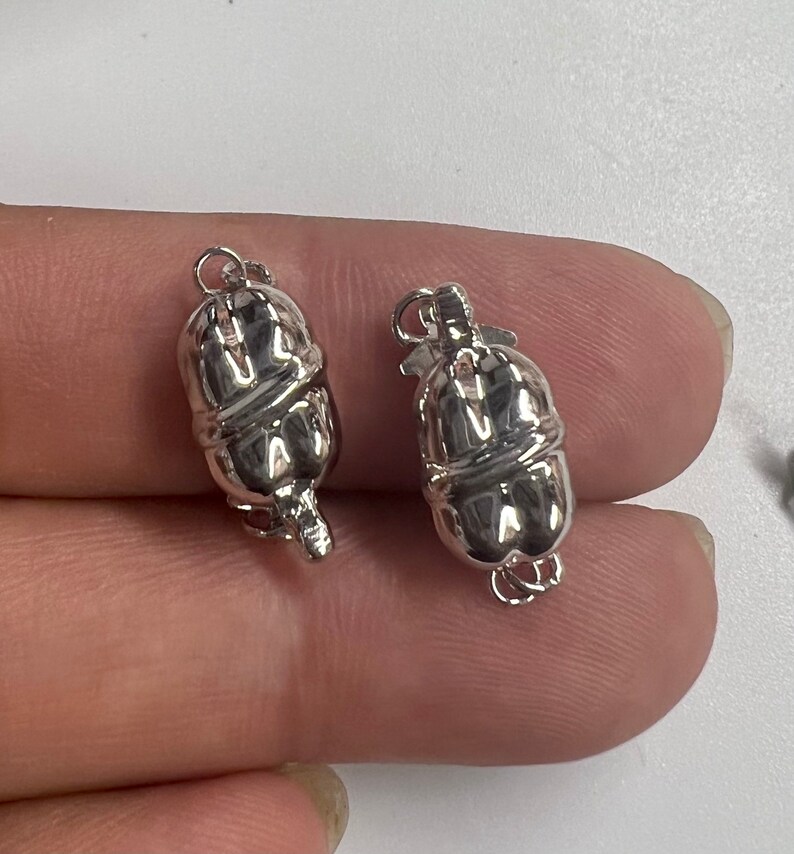 May include: Two silver-toned metal clasps for necklaces or bracelets. Each clasp is shaped like a pumpkin with a smooth, shiny finish.