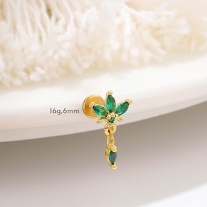 Puede incluir: Un pendiente dorado con un diseño floral, con piedras preciosas verdes. El pendiente tiene un poste y un dije colgante con una sola piedra preciosa verde. El texto "16g,6mm" es visible.