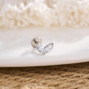 Op de afbeelding: Een zilverkleurige oorbel met een marquise-vormig, helder kristallen ontwerp. De oorbel heeft een platte achterkant en een gebogen, bladachtige kristalarrangement. De sieraden worden op een wit oppervlak getoond.