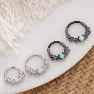 May include: Four silver and black hoop earrings with opal stones and leaf designs. The earrings are arranged in a row on a white surface.