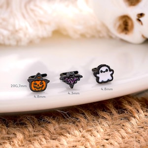 May include: Three Halloween-themed ear cuffs. The designs include a jack-o'-lantern, a bat with purple accents, and a ghost. The jack-o'-lantern and ghost are 4.8mm in size, and the bat is 4.3mm. The gauge is 20G, 7mm.