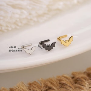 Op de afbeelding: Drie neusringen met een vleermuisontwerp. De ringen zijn zilver, zwart en goud. De dikte is 20G/0,8 mm en de lengte 6 mm.