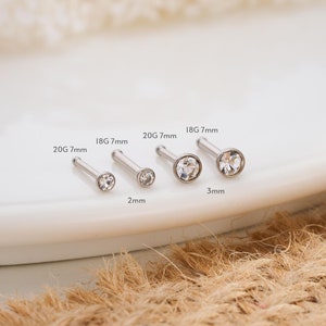 May include: Four nose rings with clear rhinestones in different sizes. The rings are labeled with their gauge and length: 20G 7mm, 18G 7mm, 20G 7mm, and 18G 7mm. The rhinestones are 2mm and 3mm in diameter.
