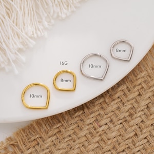 May include: Four different sizes of gold and silver seamless clicker rings with a teardrop shape. The rings are labeled with their size in millimeters: 8mm, 10mm, 8mm, and 10mm. The rings are on a white surface.