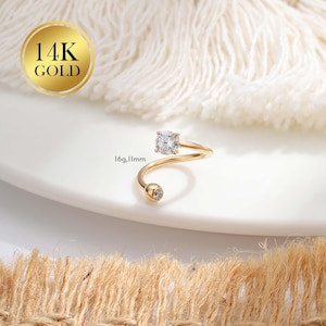 May include: A gold-colored, spiral-shaped ring with a large, square-cut, clear gemstone at the top and a smaller, round, clear gemstone at the bottom. The ring is labeled "14K GOLD" and the size is 16g, 11mm.