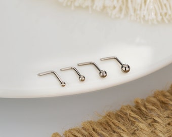 May include: Four silver nose rings with different sized ball ends. The rings are arranged in a row on a white surface.