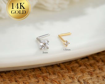 Puede incluir: Dos piercings de nariz, uno plateado y otro dorado, cada uno con una pequeña gema transparente de corte cuadrado. El piercing plateado está etiquetado como "3 mm" y el dorado como "1,5 mm". Un sello dorado dice "14K GOLD".
