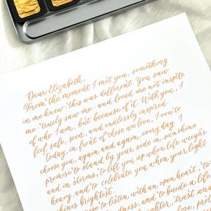 Letra caligráfica personalizada con tinta dorada en caligrafía moderna: votos matrimoniales escritos a mano, nota de amor o poema de recuerdo personalizado.